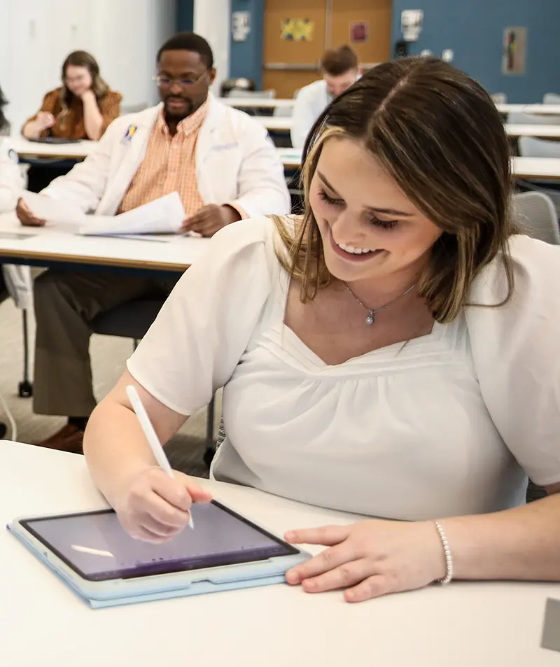 PCOM students smiling as they take notes in a biomedical sciences class