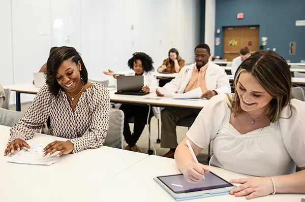 Two smiling biomed students are shown in a classroom with medical students.