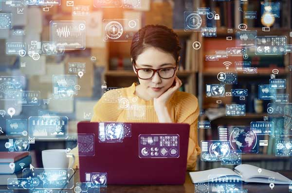 A female medical student surrounded by holographic images looks at her laptop.