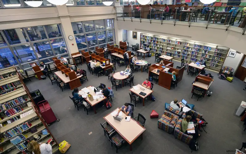 Overhead view of large room with students studying at work stations and shelves of books lining the walls