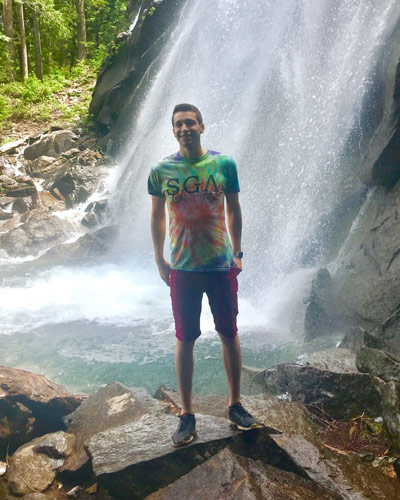 PCOM Georgia biomedical sciences graduate Hunter Alberto Vasquez, MS/Biomed ‘21, standing in front of a waterfall