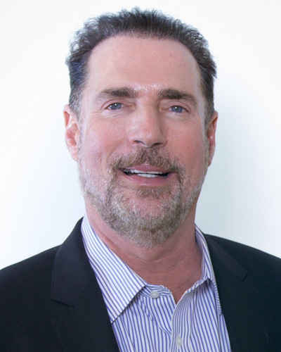 Headshot photograph of PCOM alumnus Howard A. Hassman, DO '83, smiling and wearing a blazer