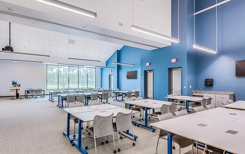 Large, open classroom with tables, chairs, projector screens and lots of natural light